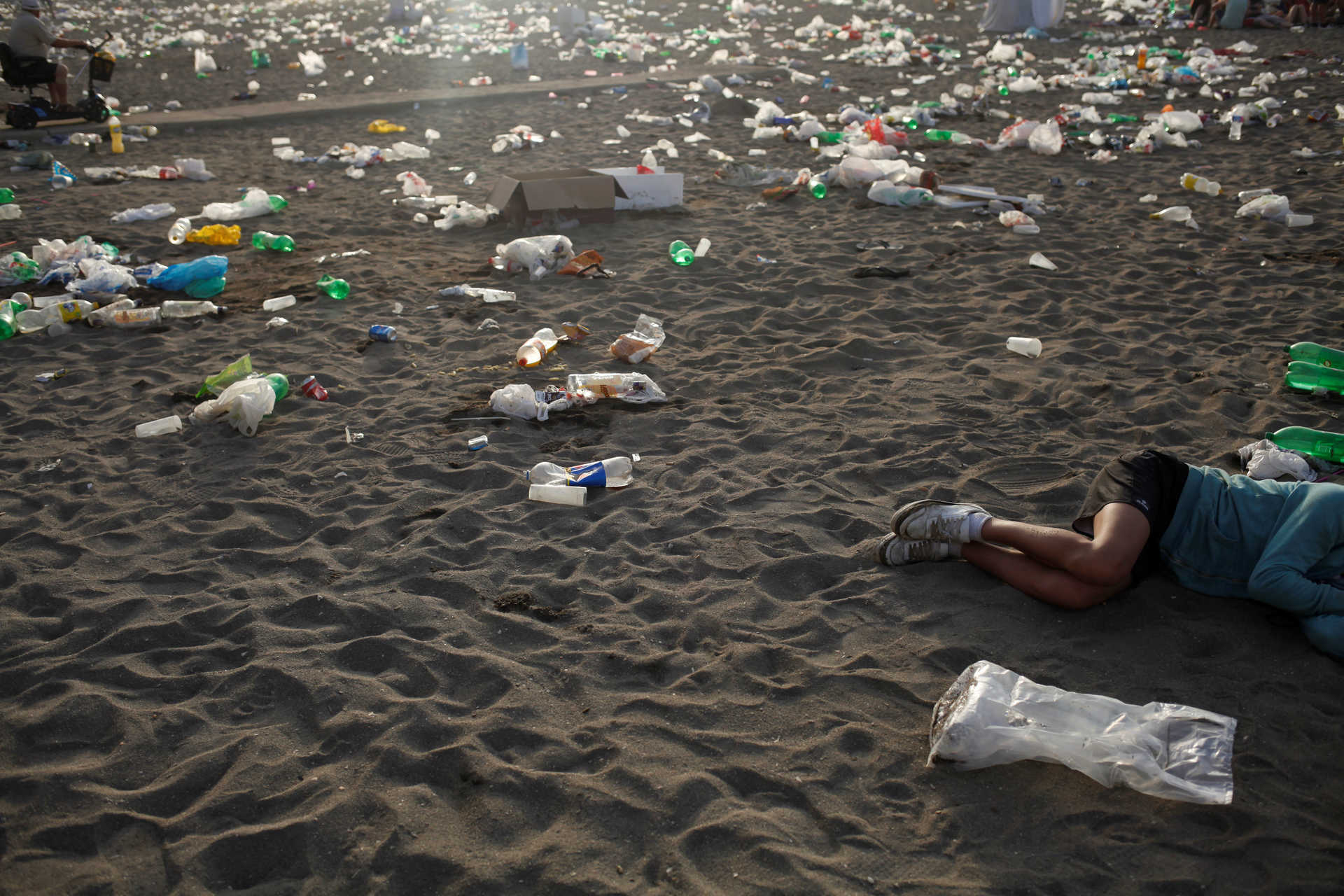 A young man sleeps surrounded by rubbish at dawn at Malagueta beach after celebrating the summer solstice in Malaga